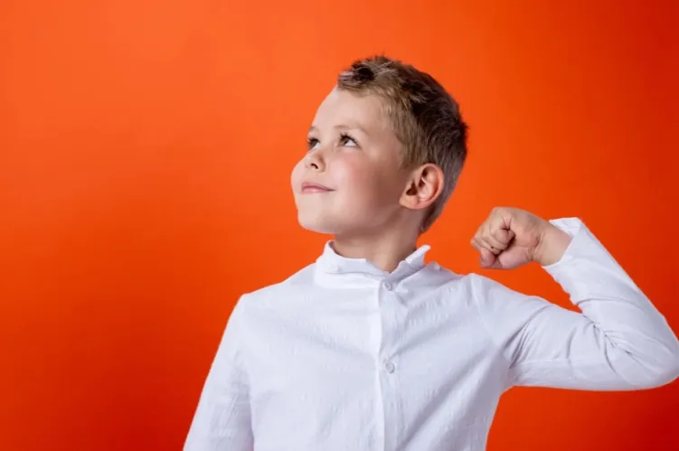 zadowolony chłopiec uczeń w białej koszuli z podniesioną reką 