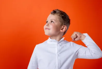 zadowolony chłopiec uczeń w białej koszuli z podniesioną reką 